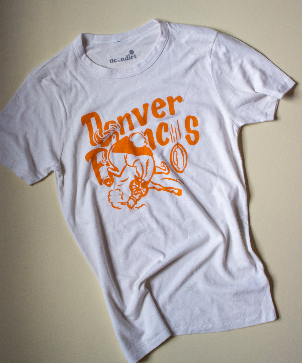 Our Forgotten and Refreshed: Denver Broncos monochrome Vintage White Tee features an orange bucking bronco centered in front of text reading "Denver Broncos". The "o" in broncos is replaced with a football icon.