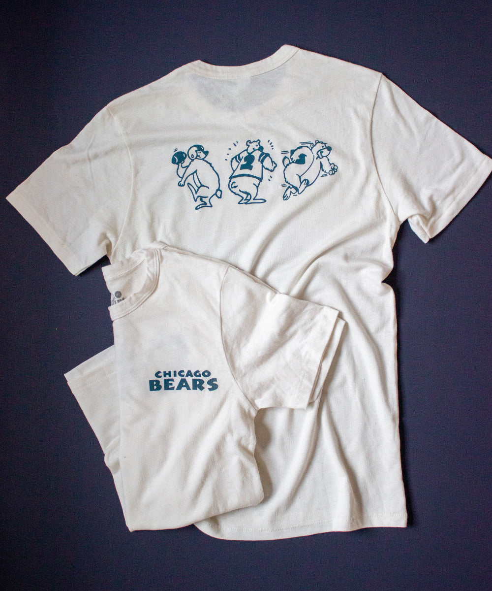Forgotten and Refreshed: Chicago Bears monochrome double sided tee. Dark blue "Chicago Bears" text spans over the upper left chest. On the back, three dark blue bear characters preform various football motions (passing, running and blocking).